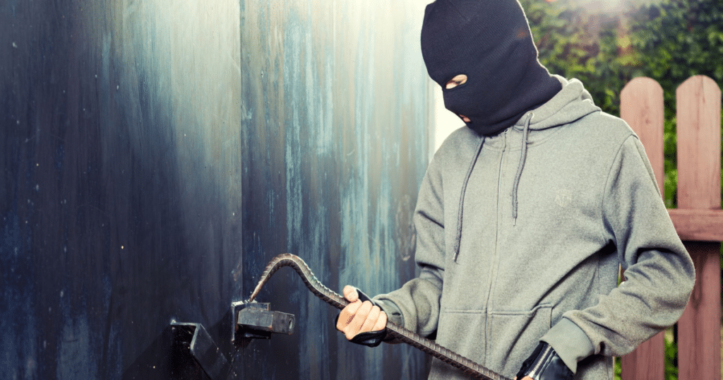 Masked person breaking a lock with a crowbar.